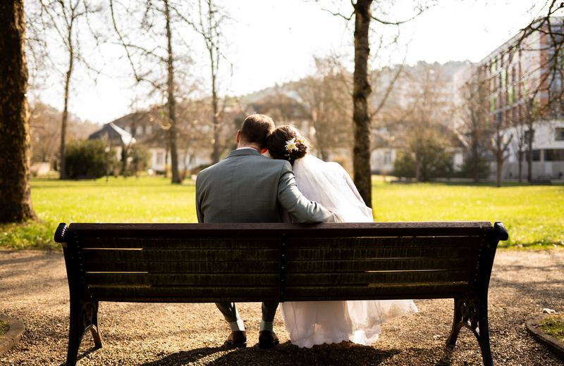 Brautpaar sitzt von hinten auf einer Bank mit Blick über den Park