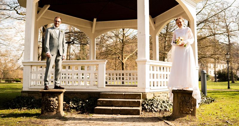 Brautpaar steht an einem weißen Pavillon im Park